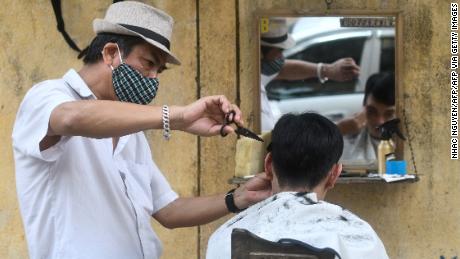 A roadside barber wearing a face mask gives a haircut to customers in Hanoi.