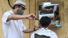A roadside barber wearing a face mask gives a haircut to customers in Hanoi.