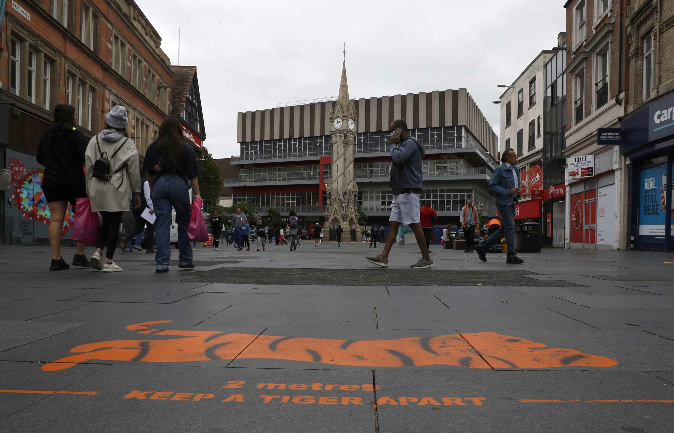 Shoppers walk past a social distancing message painted on the pavement in Leicester, England, on Monday, June 29.