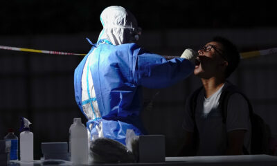 A medical worker wearing a protective suit takes a swab at a temporary test station on July 6, in Beijing.