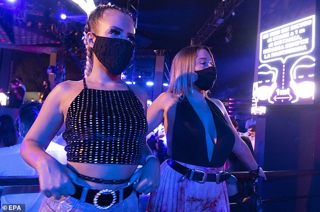 The new rules will start on Monday - two days after an Italian holiday when many young Italians go out dancing. Pictured: Two woman wearing masks dance in an Italian club, which uses its screens to remind people to wear masks and stay 1 meter apart