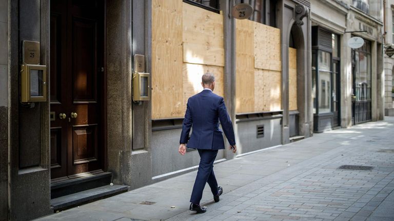 A man walks past a closed and boarded up restaurant in the City of London on August 21, 2020.