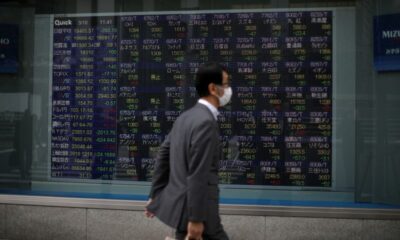 © Reuters. A man wearing protective face mask walks in front of a stock quotation board outside a brokerage in Tokyo
