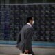 © Reuters. A man wearing protective face mask walks in front of a stock quotation board outside a brokerage in Tokyo