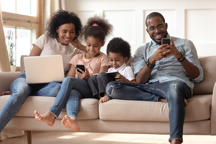 A family of four on the couch, each immersed in their own wireless device. 