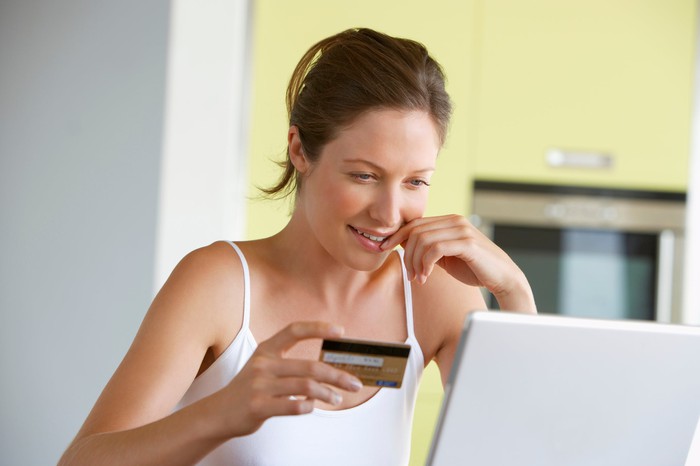 Smiling woman holding credit card in right hand looking at open laptop. 