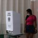 Mulher de máscara vota em uma urna eletrônica
