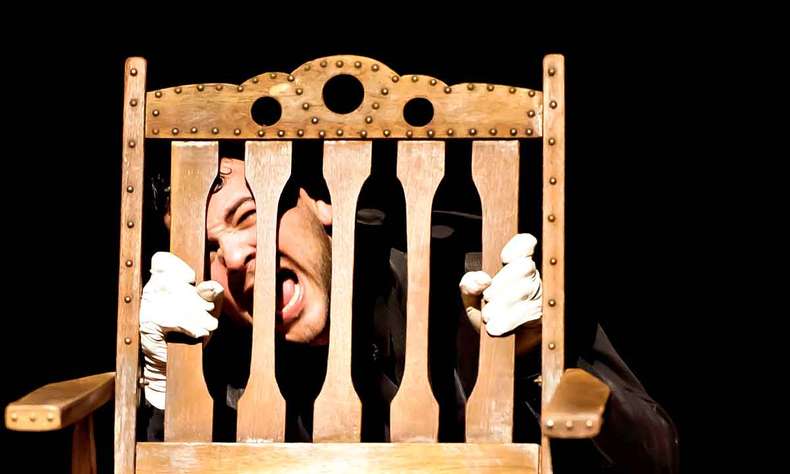 In white gloves, the actor holds on to the back of a wooden chair, glues his face to it and screams